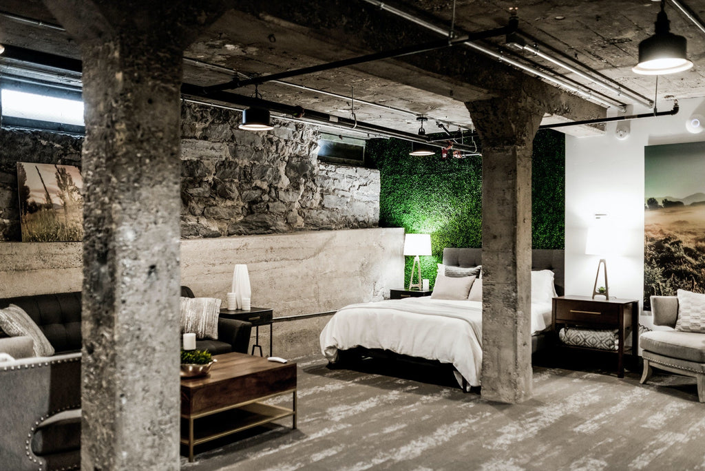 a white linen bed sitting on a basement floor 